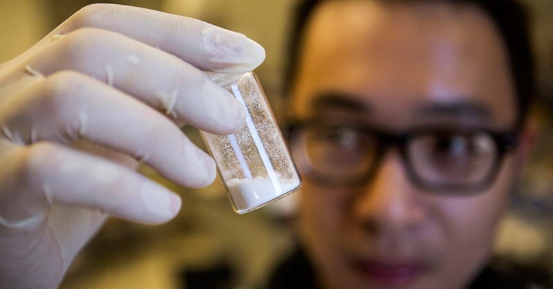 Researcher with a white gloved hand holds a capsule of white powder